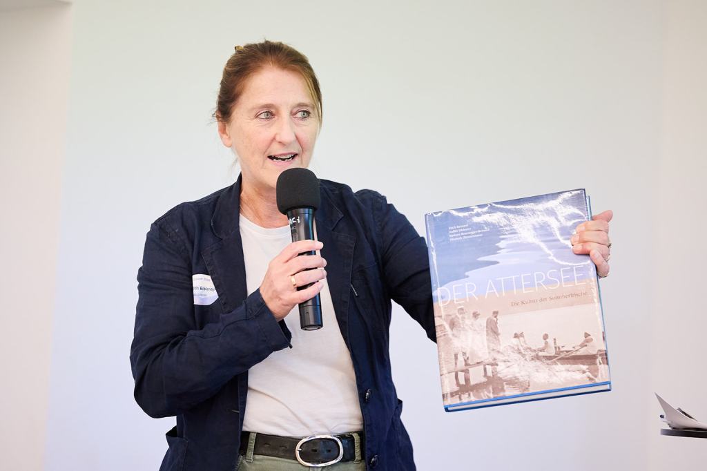 Eine Frau spricht mit einem Mikrofon und präsentiert das Buch "Der Attersee".